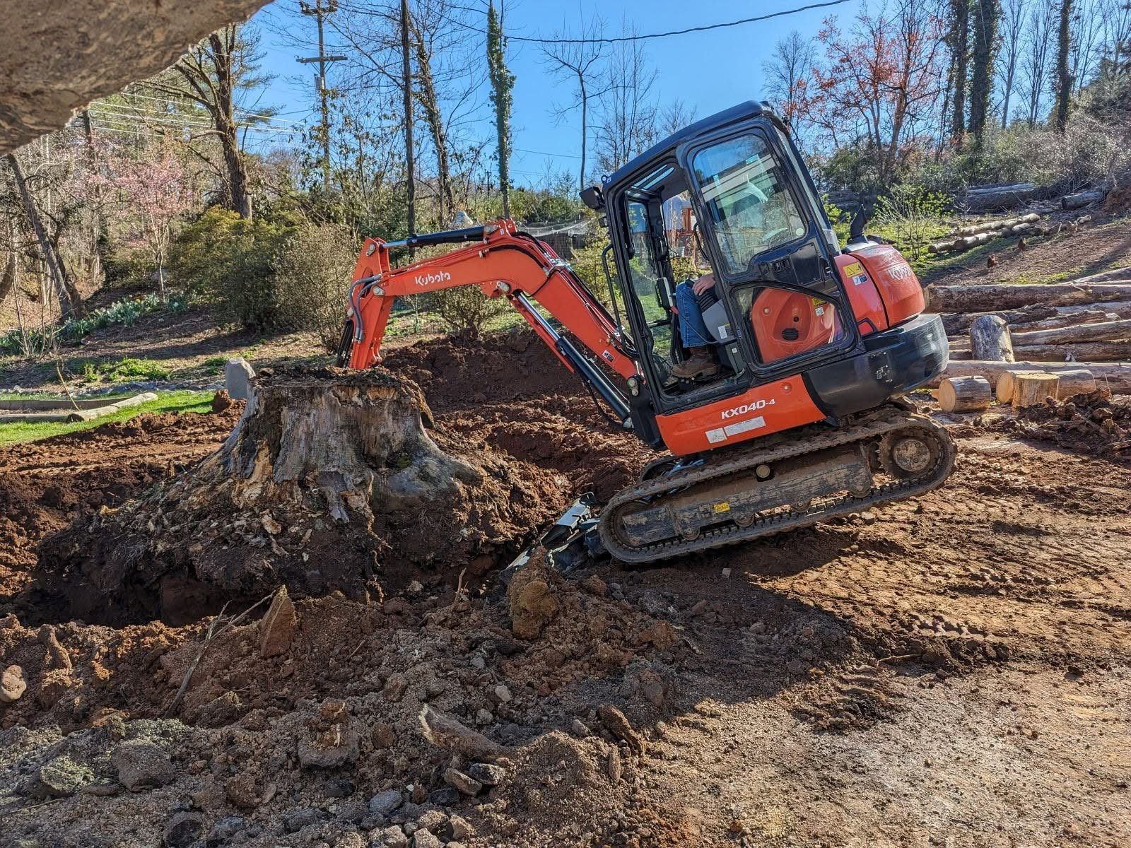 Kubota excavator working around a large root and stump mass