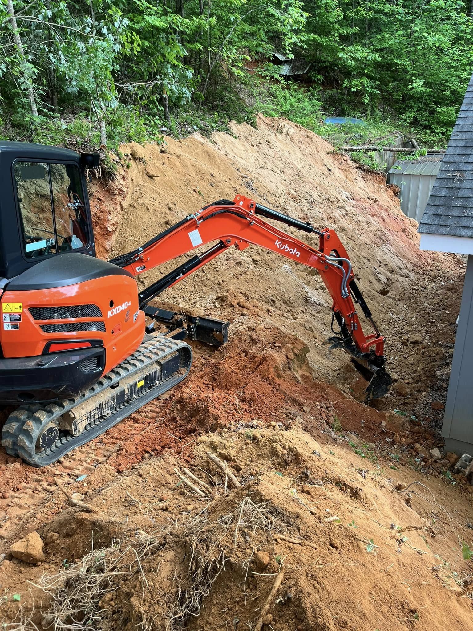 Kubota KX040-4 excavator working a steep slope beside a structure